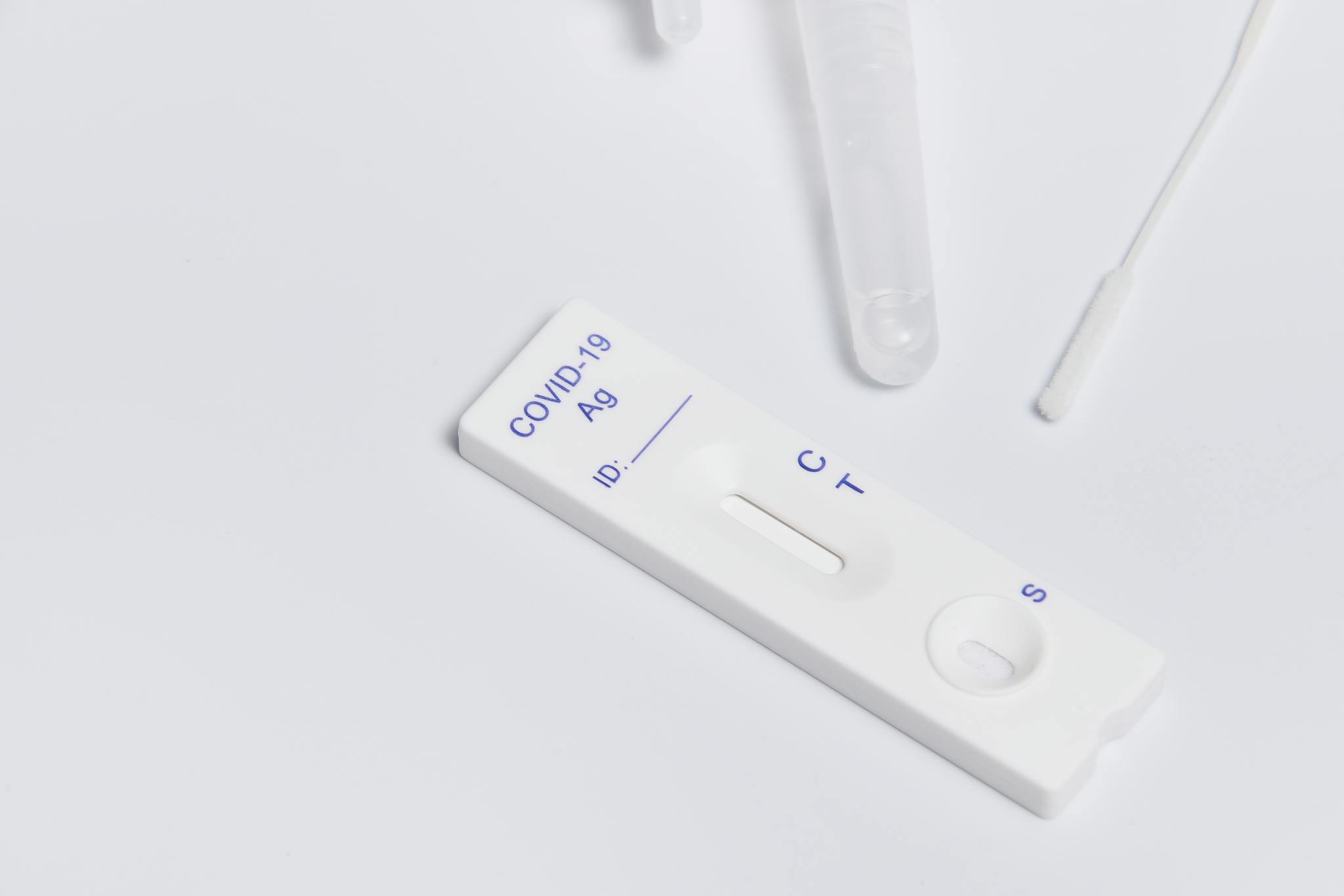 Close-up of a COVID-19 rapid antigen test kit with swab on a white surface.