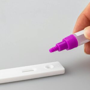 Close-up of a hand applying liquid on a rapid test kit, against a white surface.