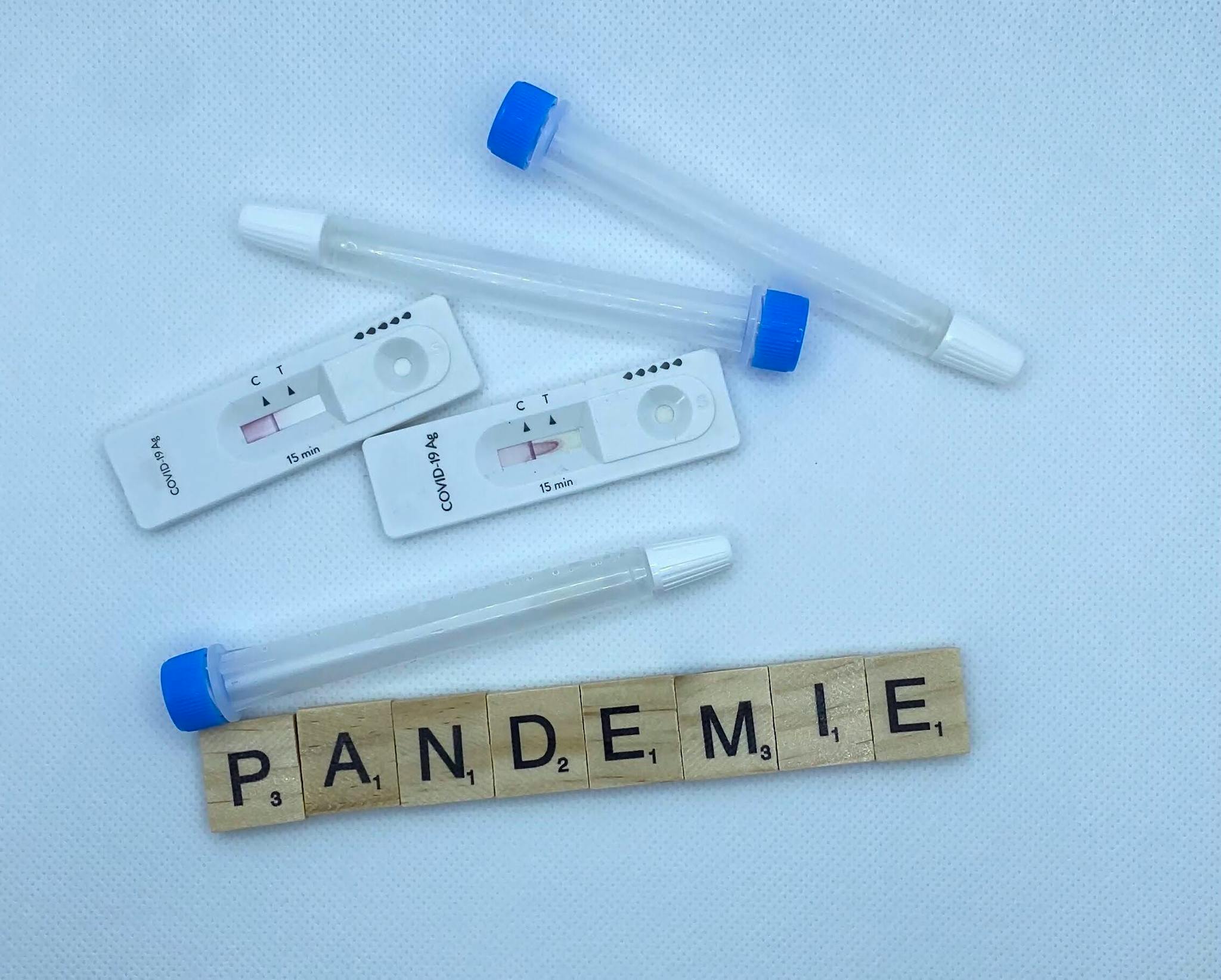 Flat lay of COVID-19 test kits with 'Pandemie' spelled out in Scrabble tiles on a white background.