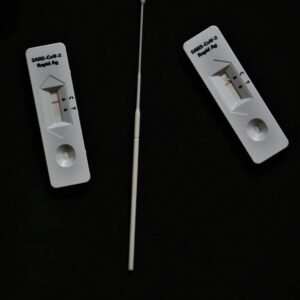 Rapid antigen test kit with swab on black surface, high angle view.